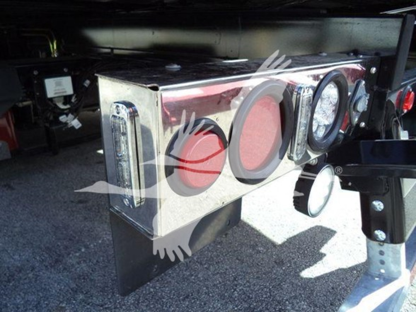 Trailer hitch or toolbox mounted on a Kenworth rollback truck showing circular red port openings and chrome housing under a trailer.