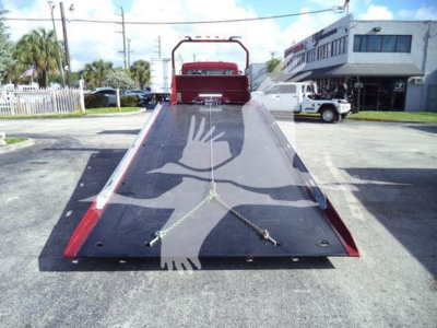 Truck tow truck with a flatbed ramp in an open lot showing rear with ramp and crossed straps.