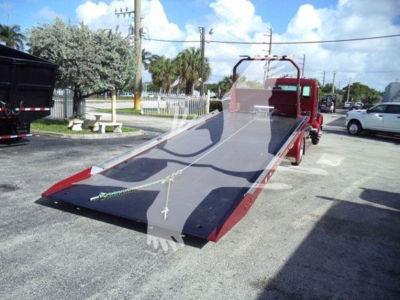 Truck roll-back flatbed with a red cab and parked in a lot. Flatbed surface visible with slight reflection and overhead power lines.