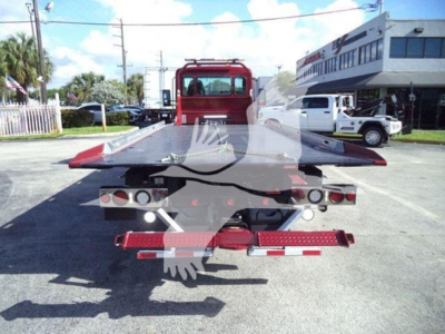 Tow truck rollback rear view showing flatbed and taillights; Kenworth T280 in background.