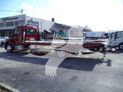 Kenworth T280 rollback truck in a dealership lot showing a red cab and flatbed tow body with a white overlay logo.