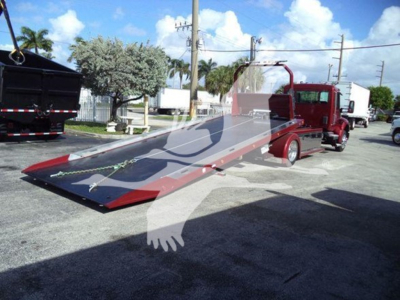 Kenworth rollback tow truck with a lowered aluminum ramp bed in sight; no legible labels visible on panels.