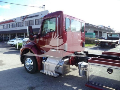 Truck cab side view showing Kenworth T-series diesel engine bay area with chrome fuel tanks and steps; rollback equipment visible in background.