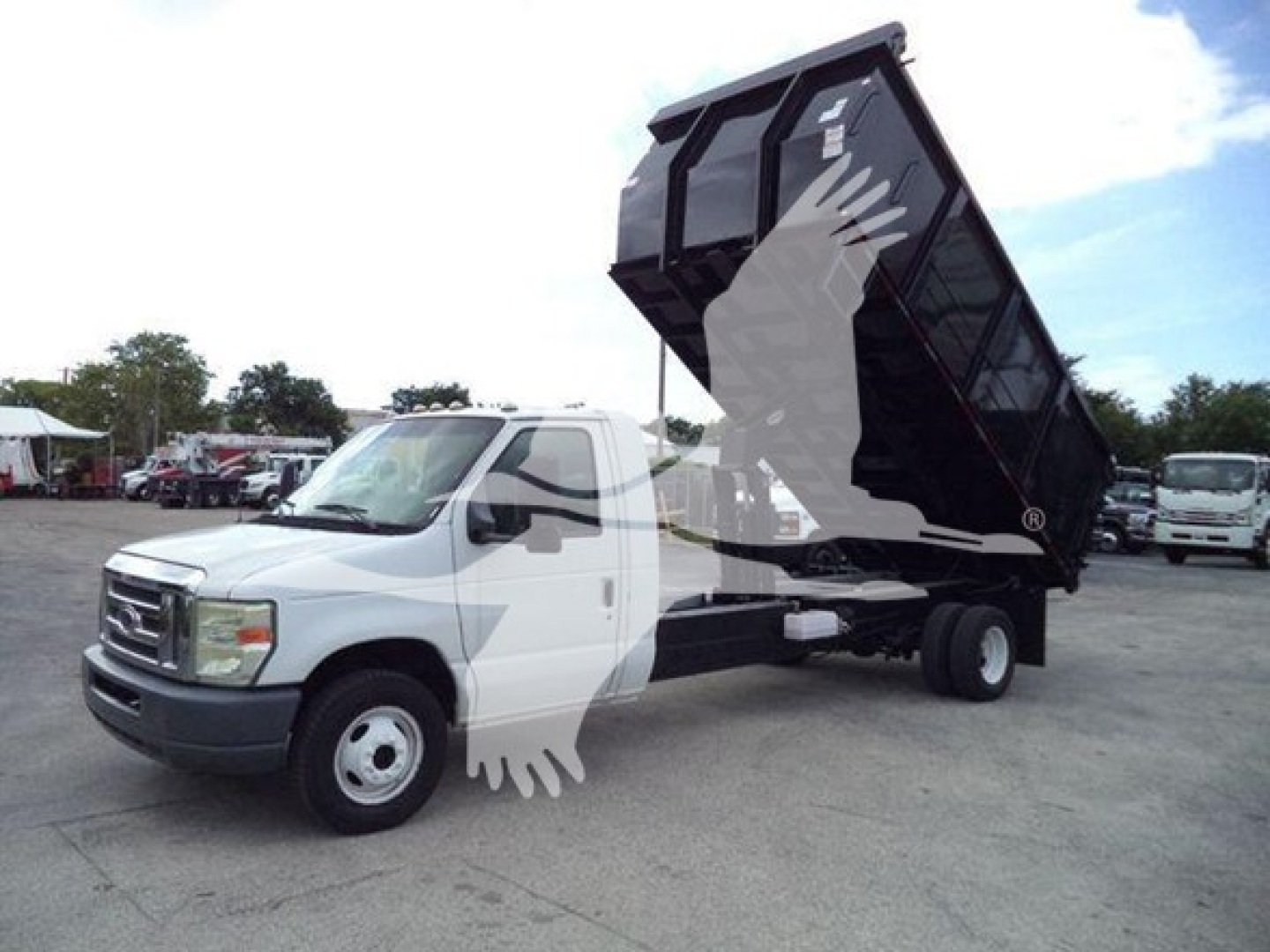 Ford E450 dump truck with raised dump bed and white cab. Side view showing front grille, wheel, and hydraulic lift.
