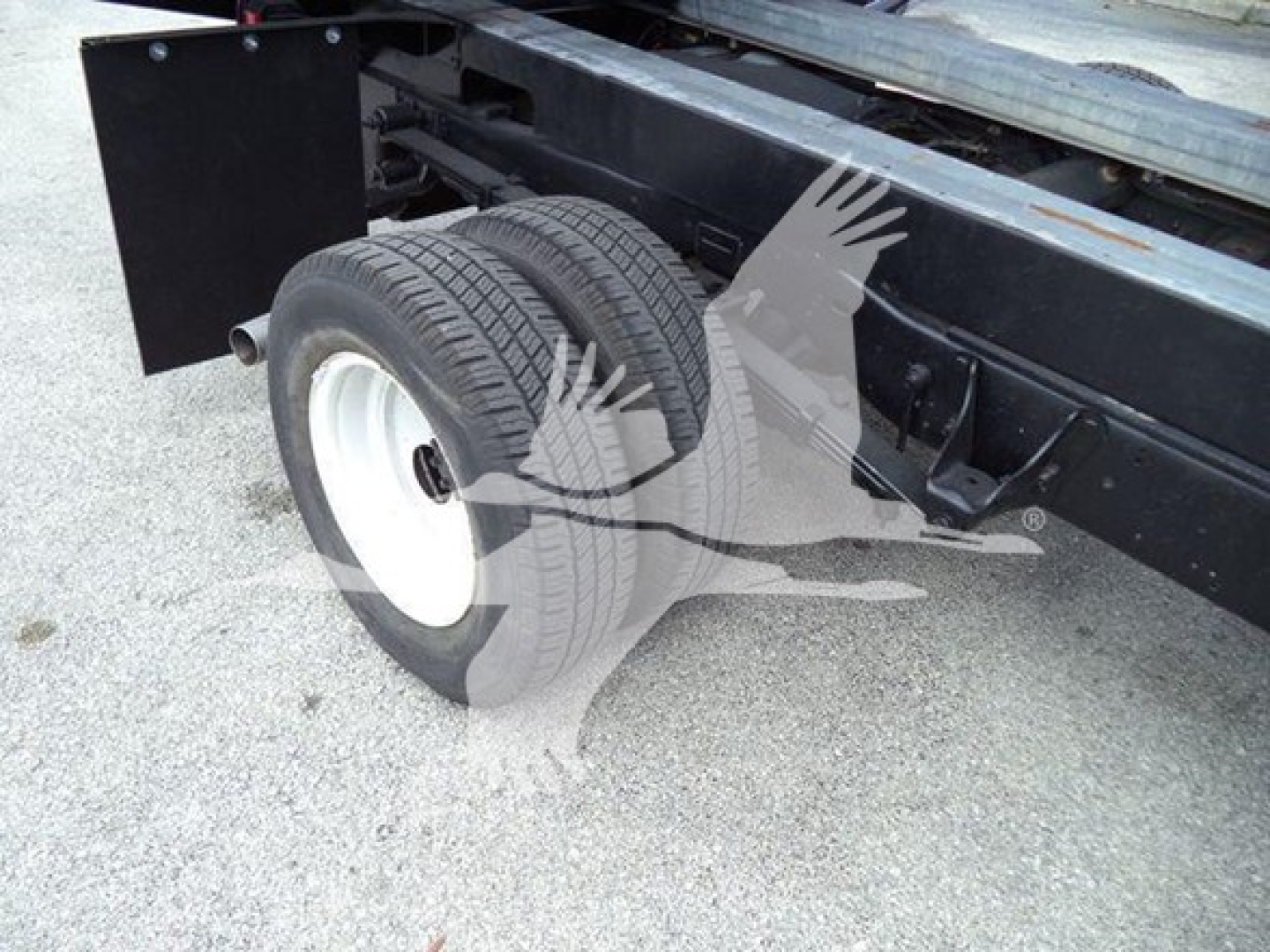 Dual rear tires on a Ford E-Series dump truck frame with undercarriage and suspension visible.