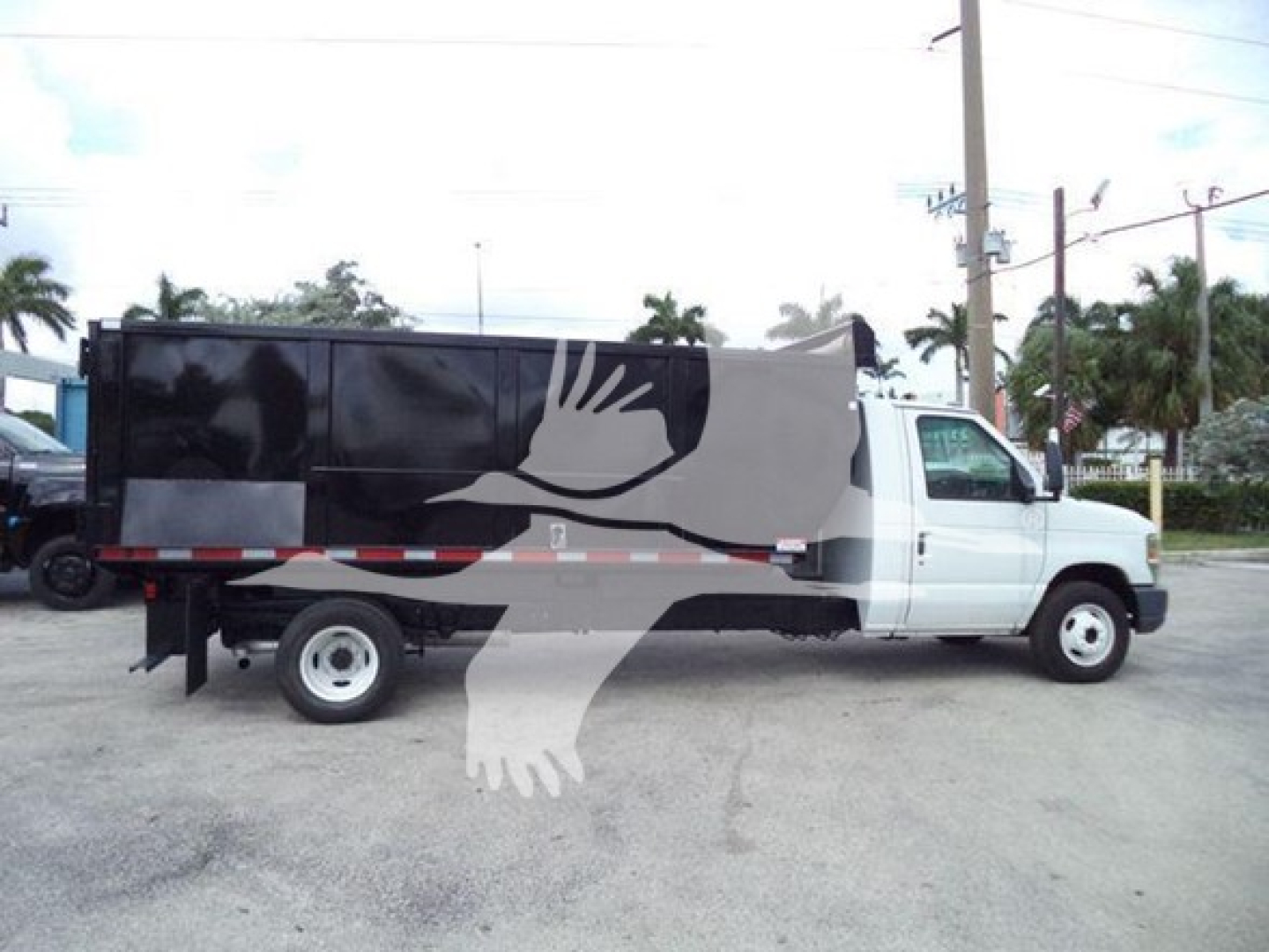 Ford E450 dump truck side view showing dump bed with black upper section and white cab.