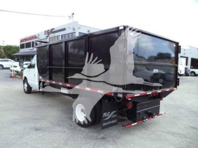 Ford E-450 dump truck with black dump body and rear tailgate, side view showing white cab and DOT reflective tape; TLC logo and contact number on rear black plate area.