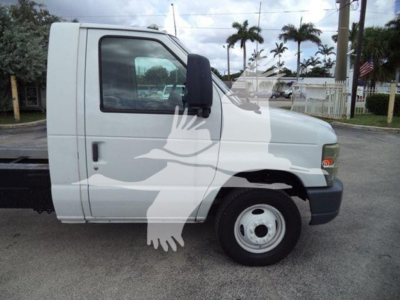Ford E450 cab side view showing single front axle with standard steel wheel and black bumper, mid-2010s model, white exterior.