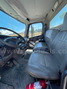 Cab interior of a Freightliner M2 106 showing driver seat, passenger bench, steering wheel, dashboard, and window views.