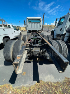 Vehicle chassis showing rear view of a Freightliner M2 106 cab and chassis with dual rear axles, metal frame, and exposed drivetrain components.