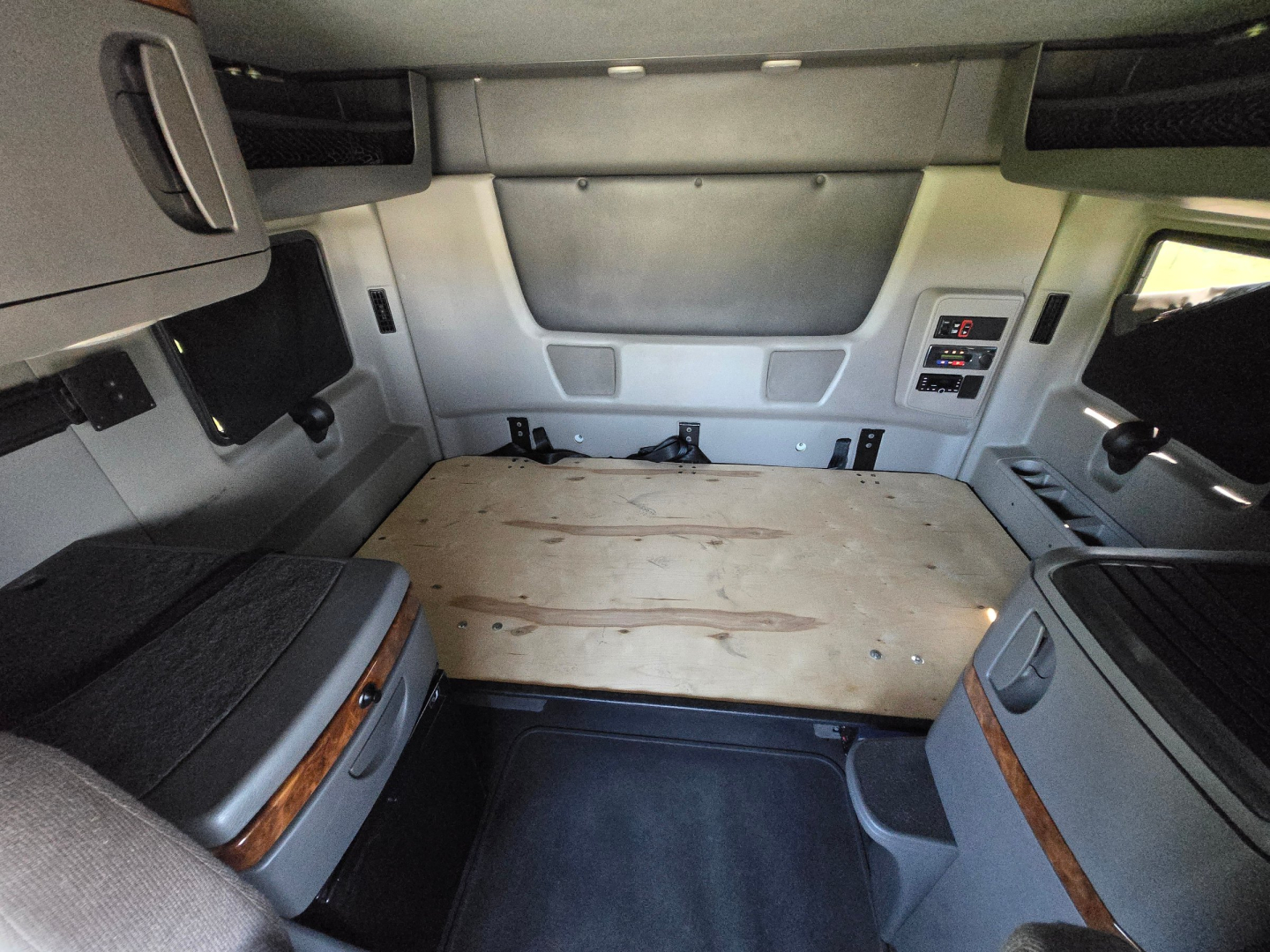 Truck sleeper cab interior cargo area with plywood bed platform and side storage compartments.