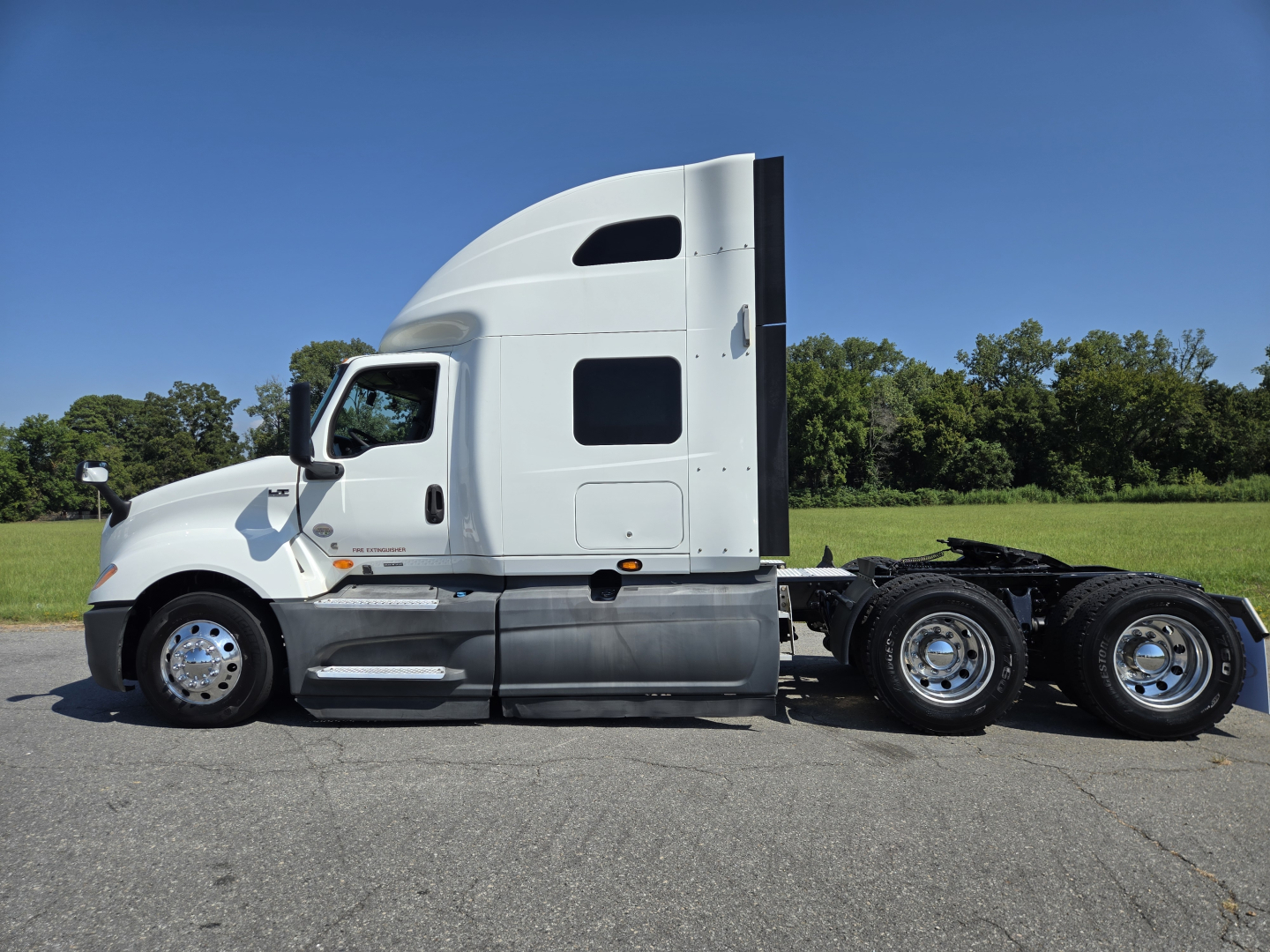 Truck cab side profile of a white 2021 International LT625 with sleeper, black wheels, and chrome fuel tanks; no visible text on the cab besides generic vehicle features.