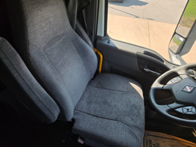 Truck interior showing driver seat and steering wheel in a 2021 International LT625 cabin. Visible are the gray fabric seat, door panel, and steering wheel with International logo.