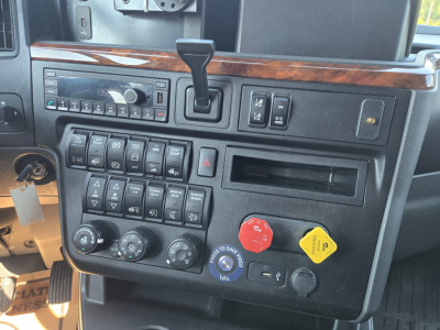 Dashboard and control panel of a 2021 International LT625 truck showing gear selector, multiple toggle switches, climate controls, and warning lights; no legible sticker text visible.