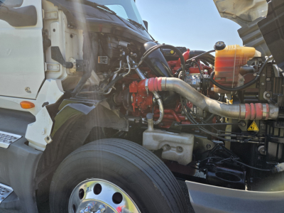 Truck engine bay of a 2021 International LT625 with visible red engine components, intake piping, and coolant reservoir.