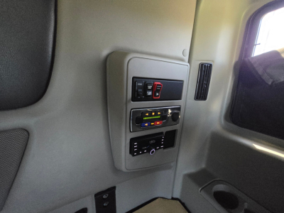 Interior of a truck cab with control panel on the wall showing switches, climate controls, and a dial; part of window and door trim visible.