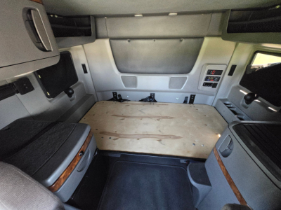 Truck sleeper cab interior cargo area with plywood bed platform and side storage compartments.