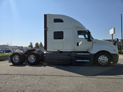 International LT-series sleeper cab tractor with white exterior, three rear axles, and chrome wheels, side profile view.