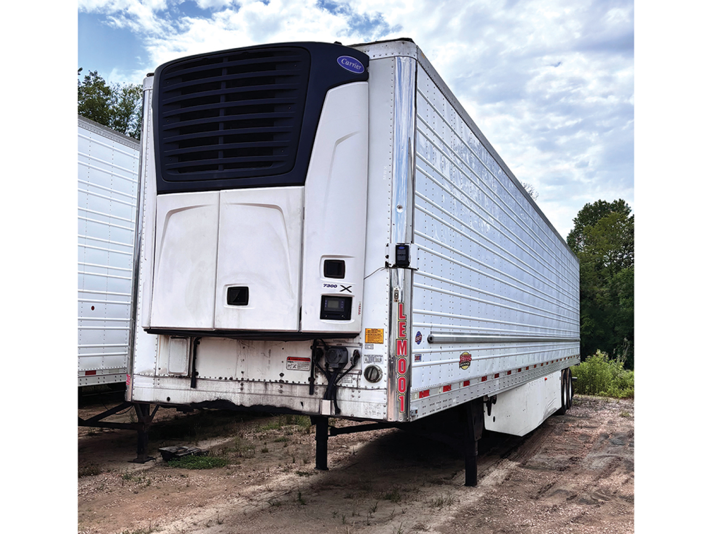 Utility 3000R trailer with a Thermo King or Carrier unit at the front, white reefer trailer, side panels, ramps underneath, parked on dirt.