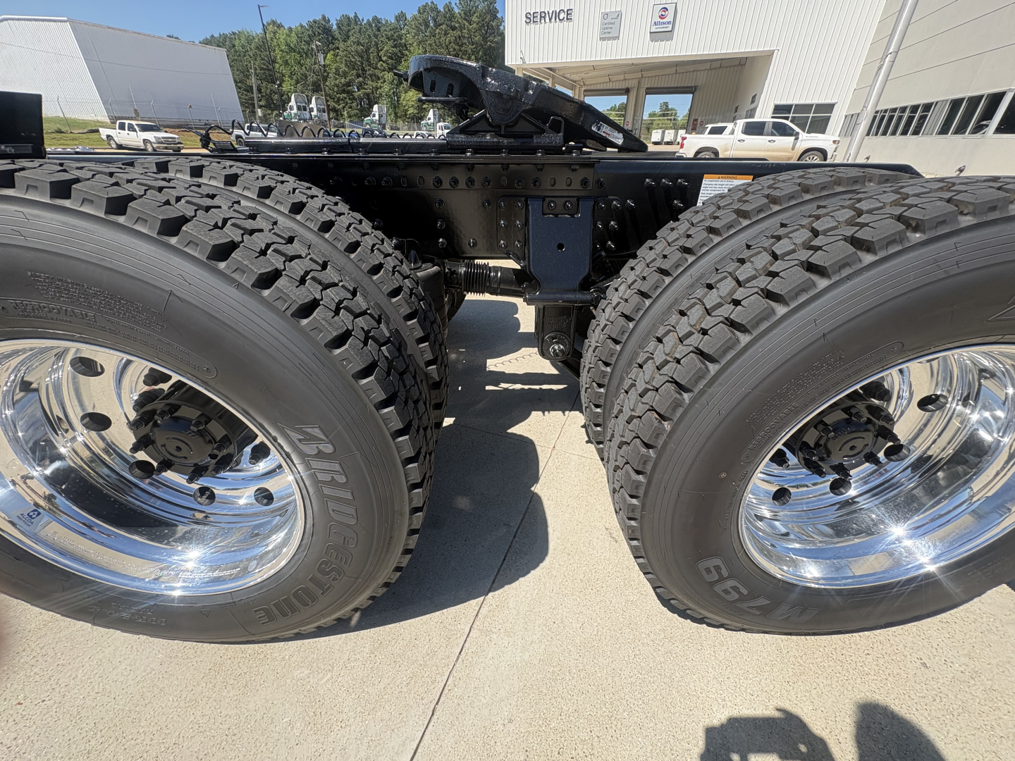 View of dual rear truck axles with large off-road tires and polished chrome rims on a Volvo VHD64FT300 chassis.