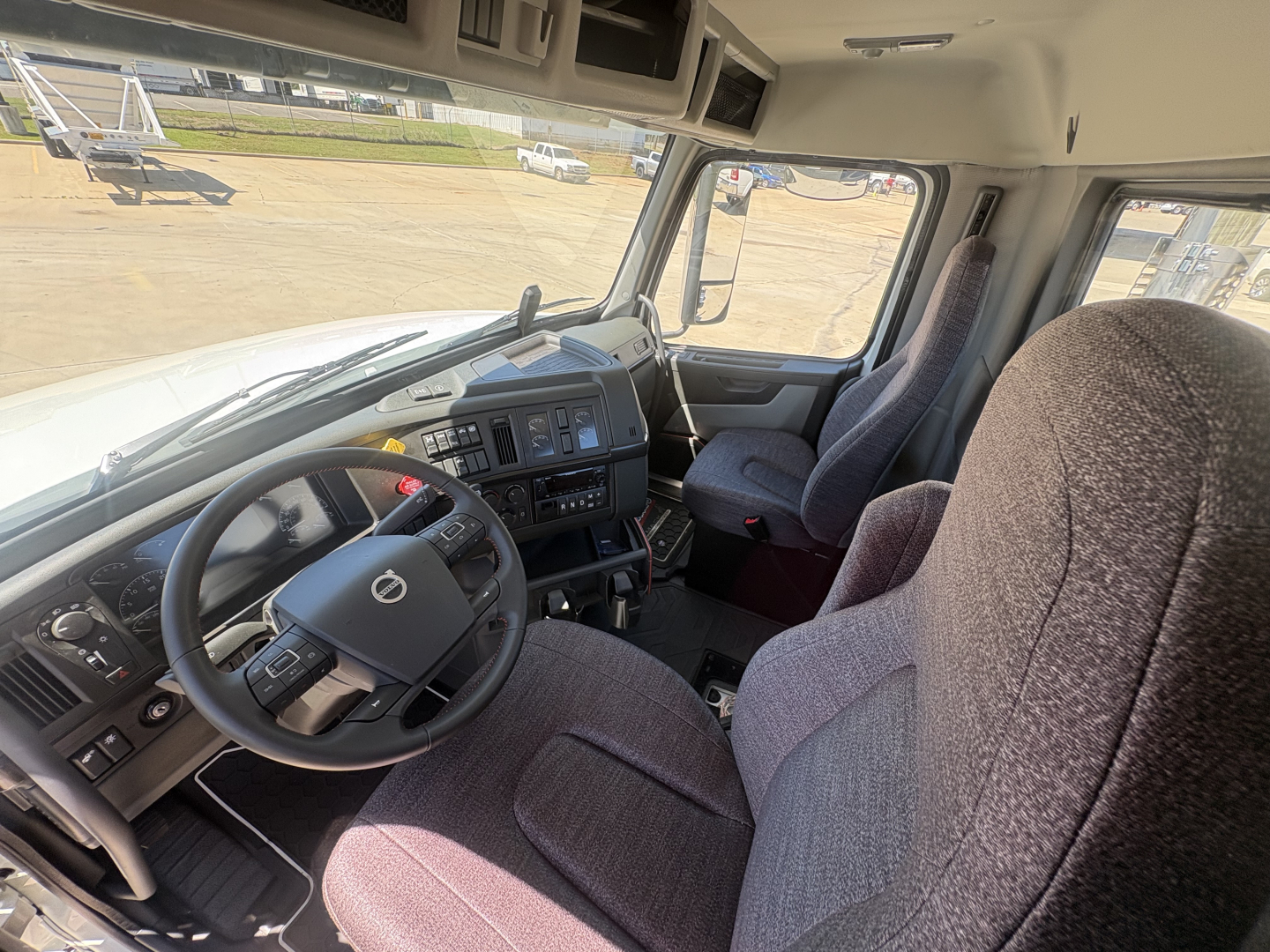 Interior view of a Volvo truck cab showing steering wheel, dashboard, and two front seats.