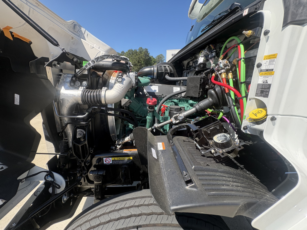 Volvo VHD64FT300 engine bay view showing coolant reservoir, hoses, and battery cables with green and red wiring visible.
