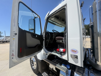 Volvo VHD64FT300 cab interior with open door showing steering wheel and driver seat; exterior door sill; chrome steps and badge; blue sky backdrop.
