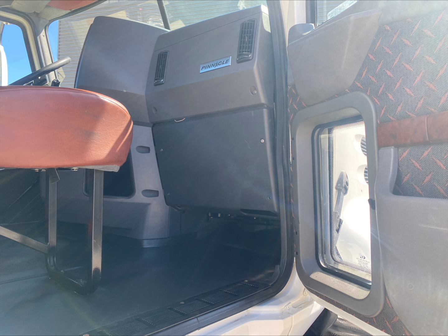 Cab interior of a 2018 Mack CXU612 truck showing dashboard area with black glovebox and seat edge.
