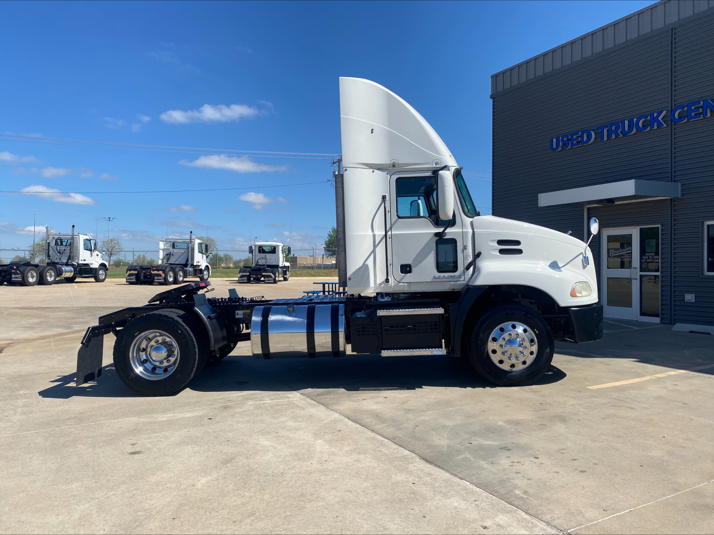 2018 Mack CXU612 conventional daycab tractor side view showing cab, fuel tanks, wheels, and chassis; white cab with blue frame and chrome wheels.