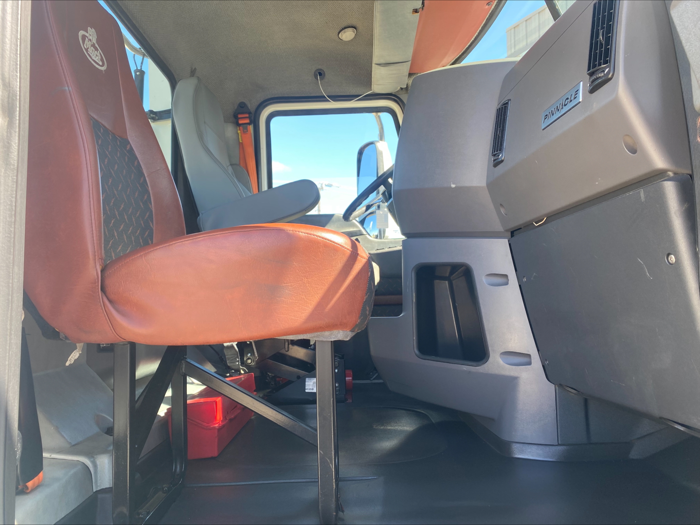 Cab interior of a 2018 Mack CXU612 daycab truck showing driver seat, passenger seat, dashboard, and steering area.