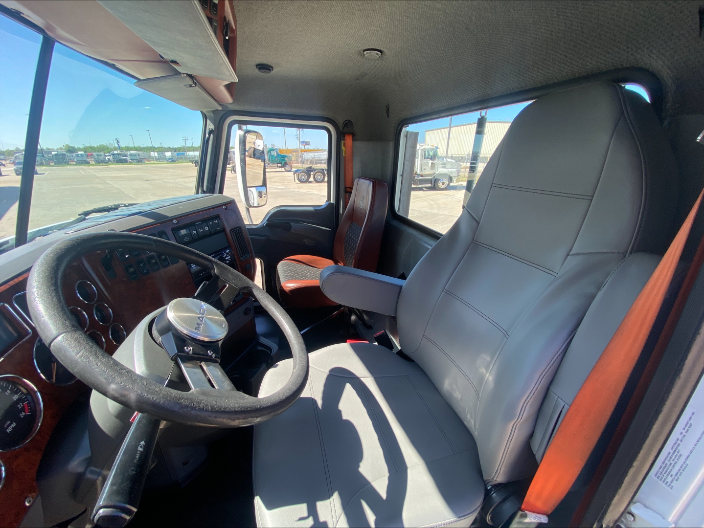 Cab interior of 2018 Mack CXU612 conventional daycab showing steering wheel, dashboard, driver seat, and passenger seat with gray upholstery.