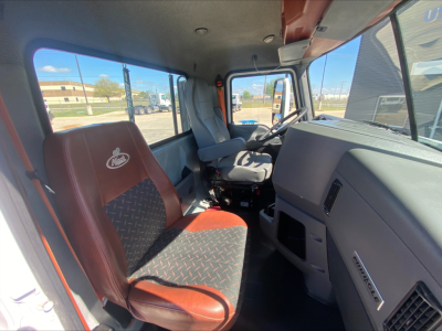 Cab interior of a 2018 Mack CXU612 daycab showing driver seat and dashboard with steering wheel; visible window and side mirror.