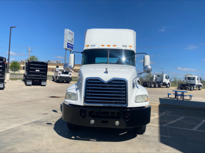 Front view of a white 2018 Mack CXU612 truck with large chrome grille, bumper, and side mirrors; parking lot with other trucks in background.