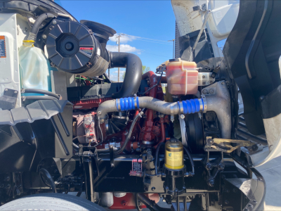 Mack CXU612 engine bay showing coolant reservoir, hydraulic lines with blue protective sleeves, yellow filter, and red engine block.