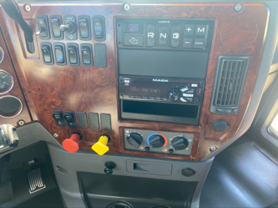 Cab interior of 2018 Mack CXU612 showing dashboard with multiple switches, MACK radio unit, climate controls, and woodgrain panel.