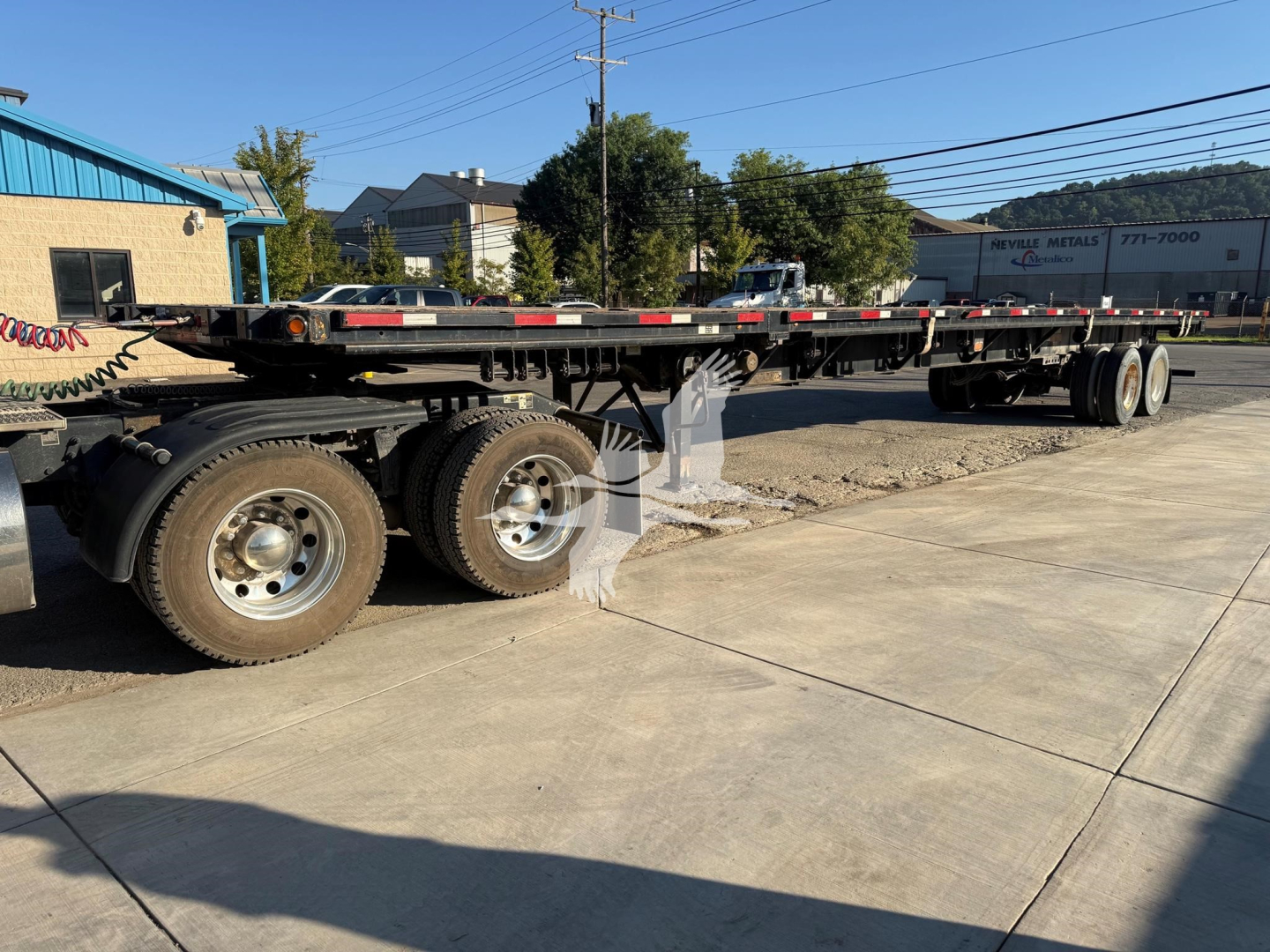 Flatbed trailer showing wheels and undercarriage with multiple axles and reflective tape.