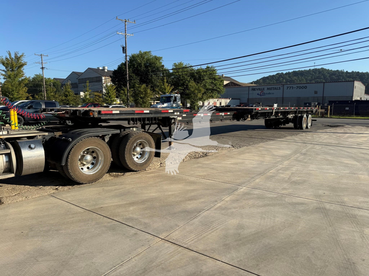 Flatbed trailer showing tandem axles and long gooseneck at an outdoor lot with multiple trailers in background.