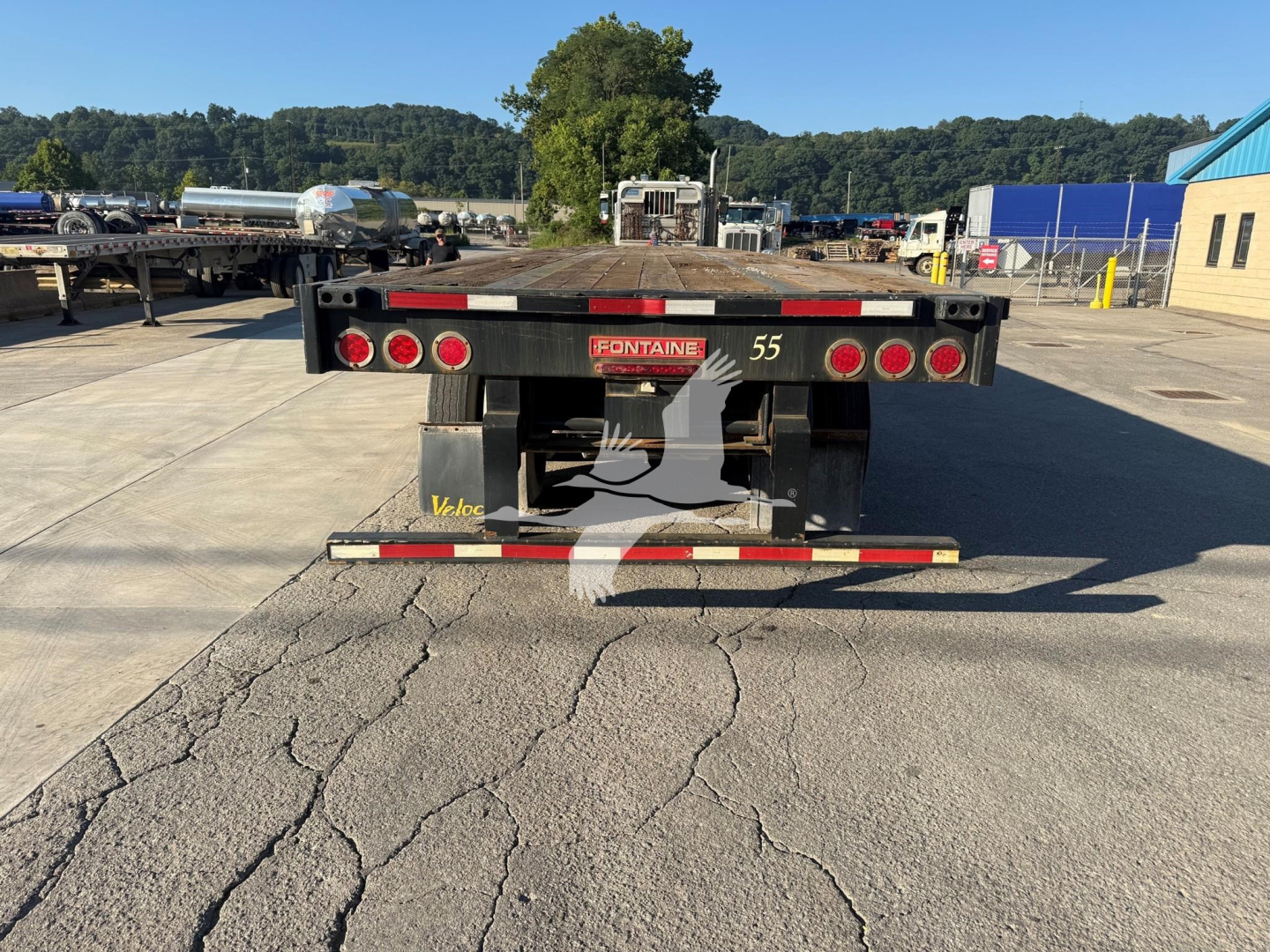 Flatbed trailer rear view showing Fontaine balance and taillights with bumper and license plate area, 55 printed on side, stock lot in background.