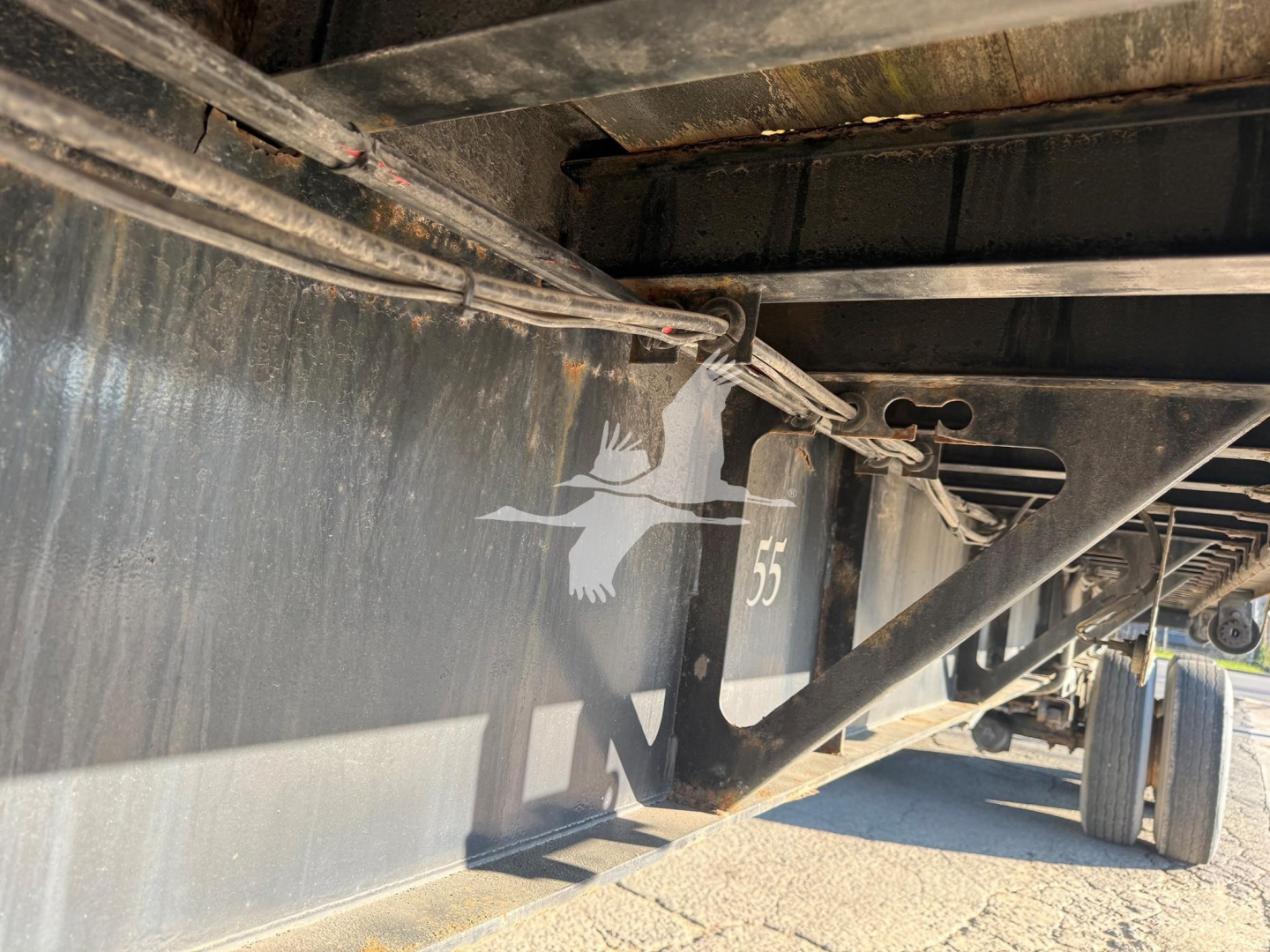 Trailer undercarriage with steel frame and wiring harness, Fontaine logo visible on side panel, wheel and part of flatbed structure in view.