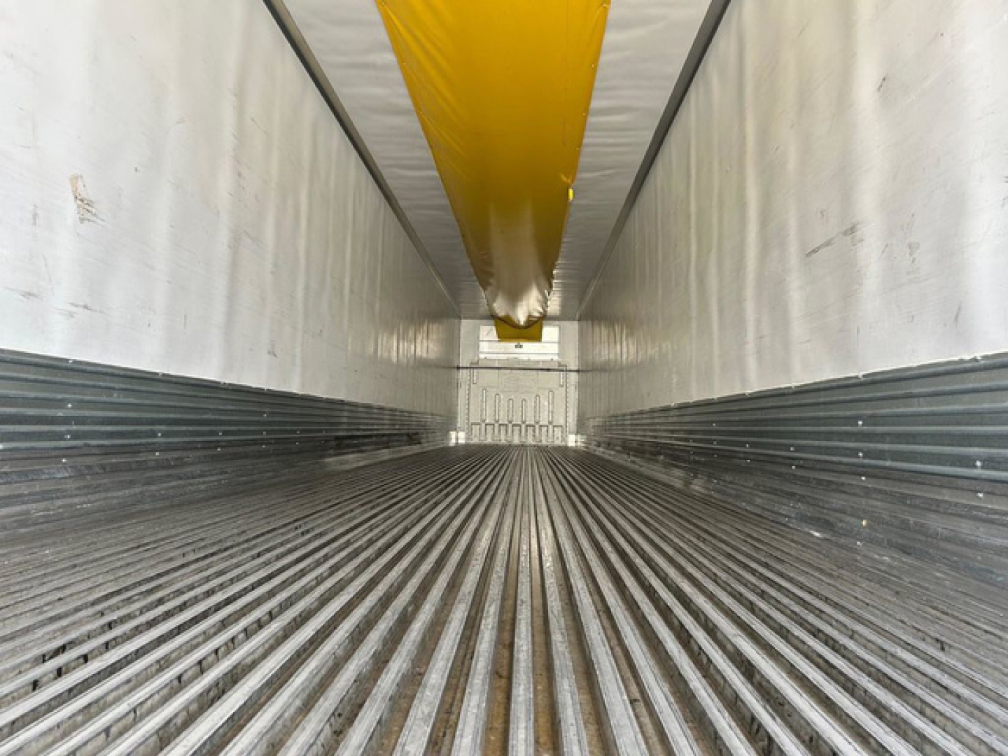 Trailer interior showing refrigerated trailer with ribbed floor and yellow ceiling beam, side walls in view