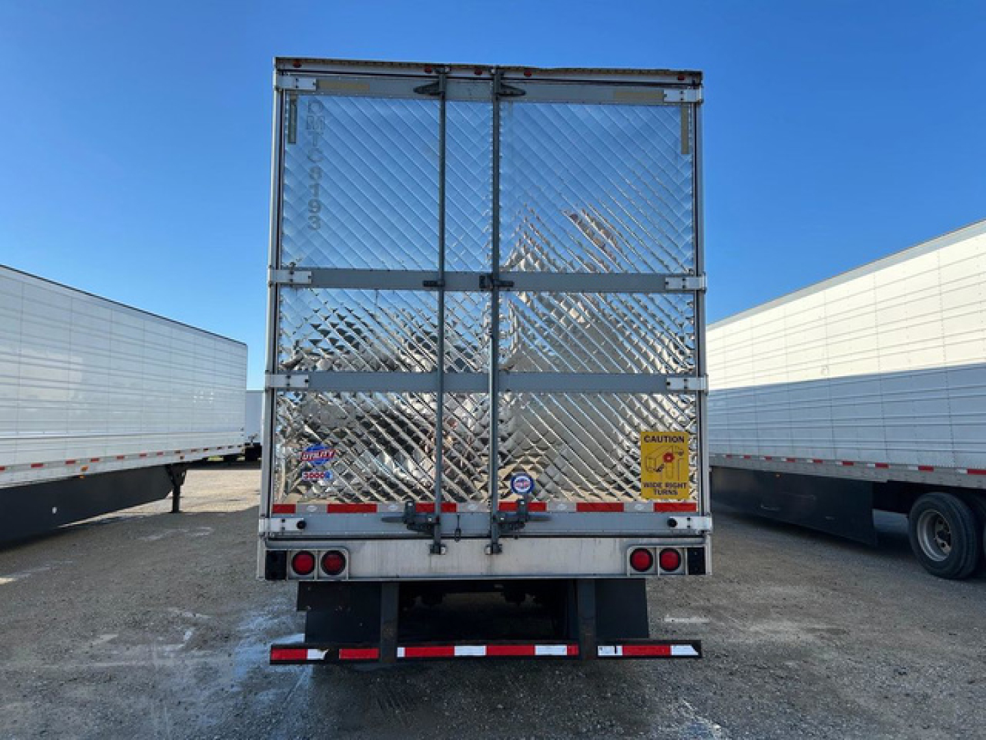 Rear view of a 2016 utility refrigerated trailer with diamond-plate doors, safety decals, and taillights, parked among other trailers.