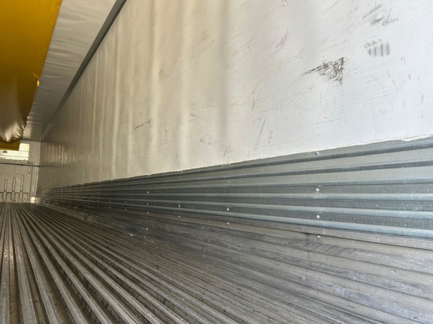 Trailer interior showing ribbed steel floor and side wall with yellow upper structure; worn marks along wall.