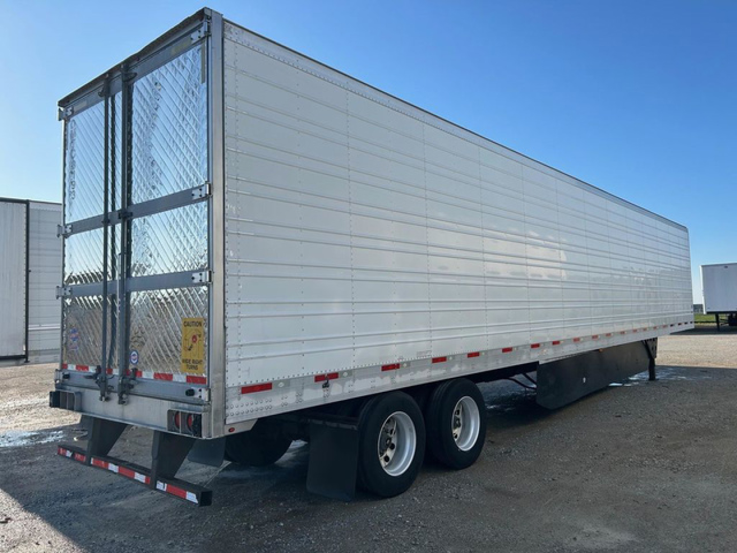 Utility reefer trailer side and rear showing white aluminum panels, dual rear axles, rear doors with diamond plate gate, and reflective safety stripes.