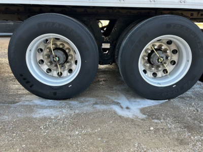 Trailer dual tires showing wheel rims and suspension undercarriage with snow and ice on ground.