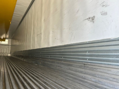 Trailer interior showing ribbed steel floor and side wall with yellow upper structure; worn marks along wall.