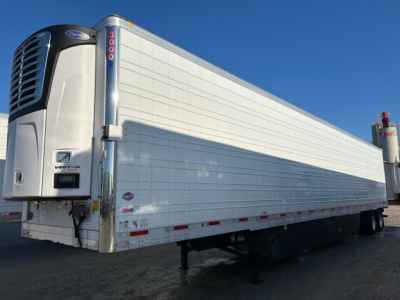 Utility trailer with a refrigerated unit at the front; side shows riveted aluminum panels and a vertical rear door with red numbers; blue sky above.