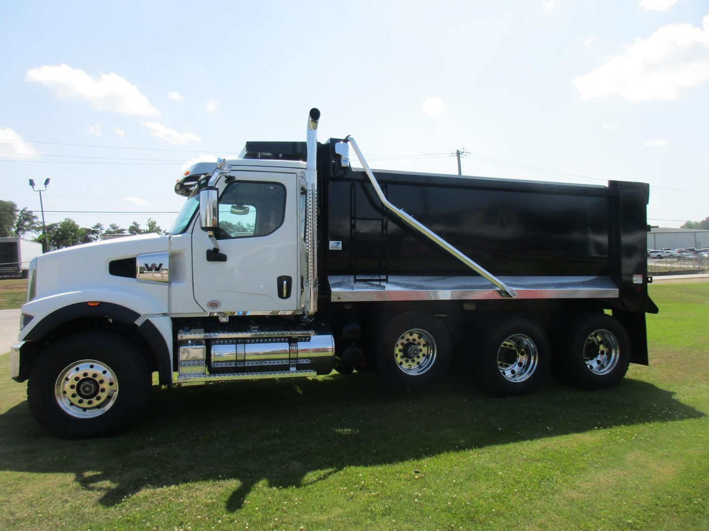 Truck side view showing a white Western Star 49X dump truck with a black dump bed, chrome accents, and triple rear axles.