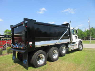 Western Star 49X dump truck shown from rear three-quarter view with black dump bed and dual rear axles on a grassy lot.