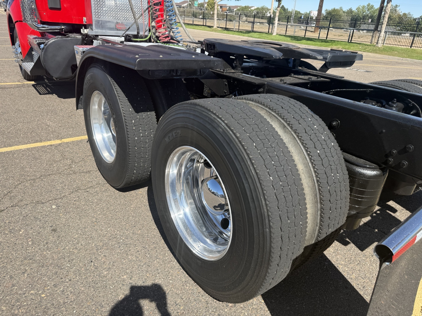 Kenworth T880 chassis showing dual rear axles with chrome wheels and tires, front view of axle area, red cab in background.