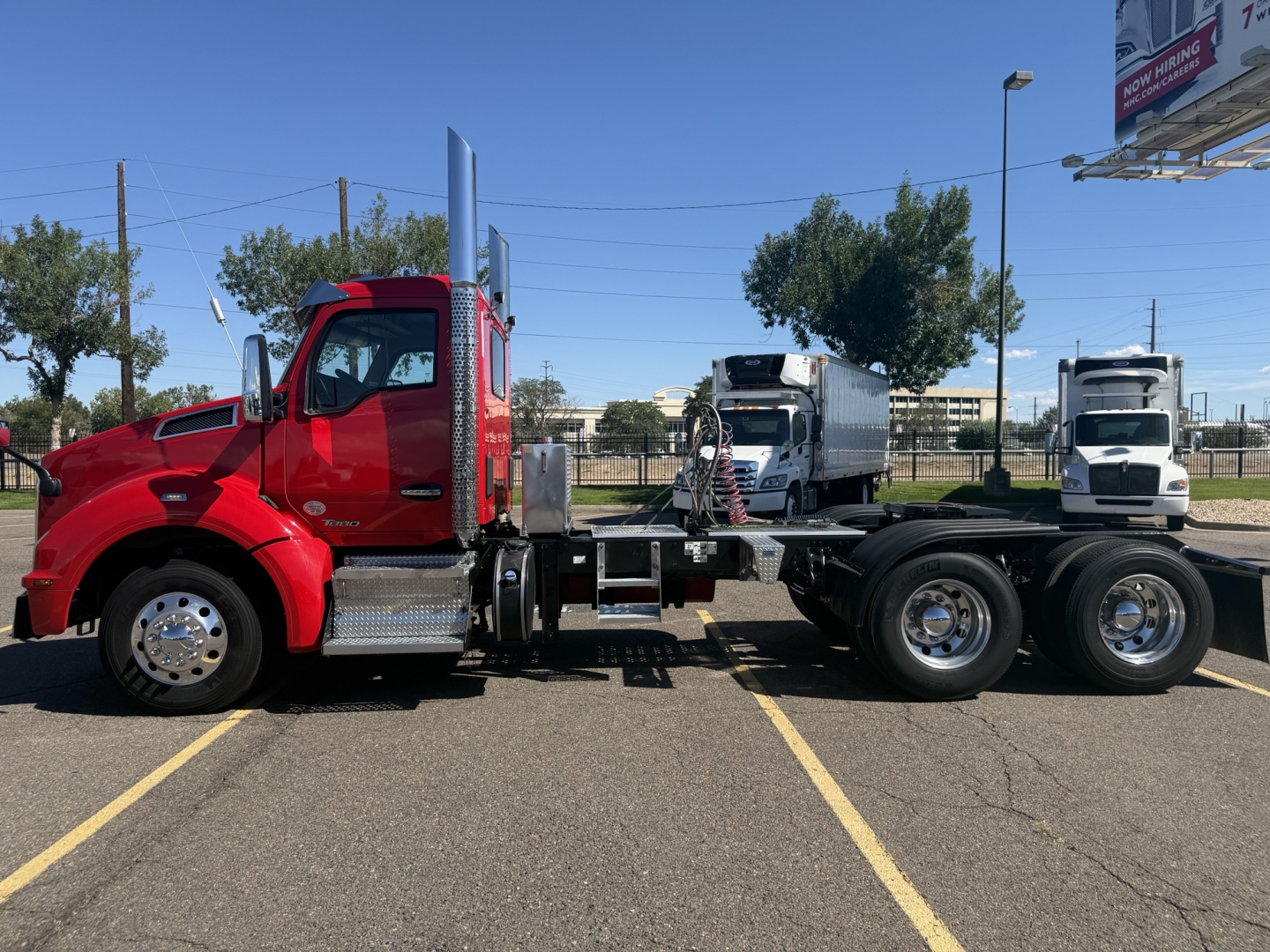 Kenworth T880 chassis cab side view in red with long wheelbase and dual rear axles in a parking lot.